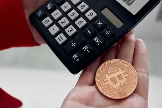 Руки держат калькулятор и золотую монету биткоин