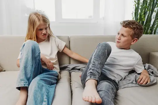 Двое детей в повседневной одежде сидят на бежевом диване в светлой гостиной