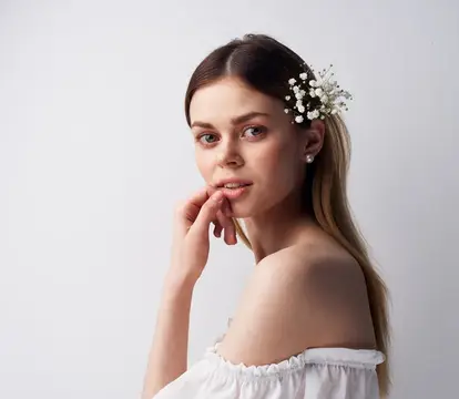 Молодая женщина с цветами в волосах застенчиво улыбается на светлом фоне