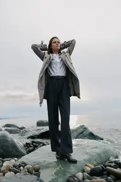 Молодая женщина в плаще стоит на камнях у моря