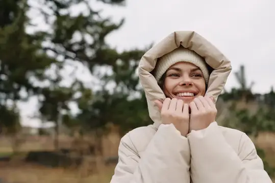 Улыбающаяся девушка в светлом пуховике с капюшоном на природе