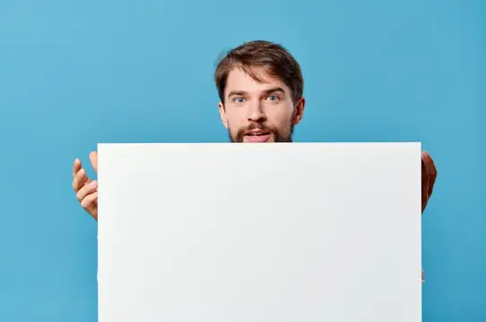 Удивлённый бородатый мужчина выглядывает из-за белого листа на синем фоне