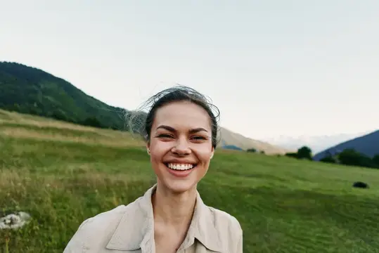 Улыбающаяся темноволосая женщина на фоне зелёных гор и луга