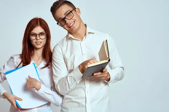 Улыбчивые парень и рыжеволосая девушка в очках с книгами и папкой