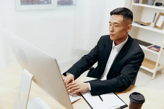 Азиатский мужчина в костюме работает за компьютером в офисе