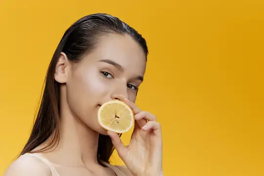 Молодая женщина с долькой лимона у лица на жёлтом фоне