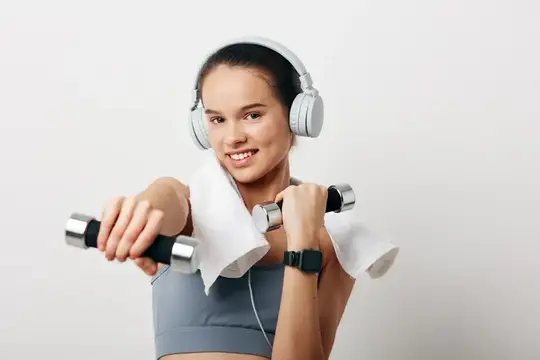 Улыбающаяся девушка с гантелями и в наушниках на тренировке