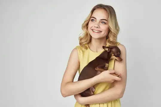 Улыбающаяся блондинка держит маленькую коричневую собачку