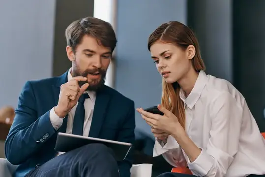 Мужчина и женщина в деловых костюмах обсуждают смартфон в офисе