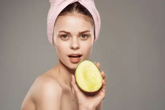 Улыбающаяся женщина с обнаженными плечами, с полотенцем на голове, держит манго в руке, обрезанный вид