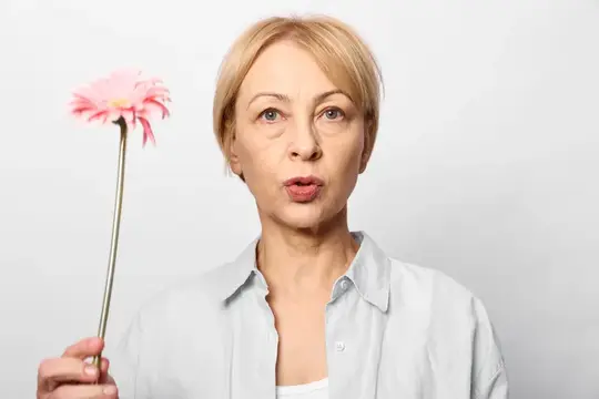 Светловолосая женщина с розовым цветком задумчиво смотрит в камеру