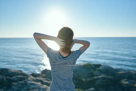 Женщина отдыхает у моря в горах на природе летом, на заднем плане закат