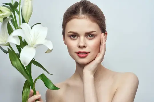 Молодая женщина с белыми лилиями в руках на сером фоне