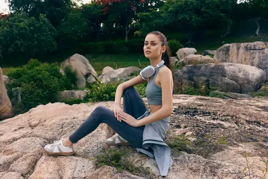 Спортивная девушка с наушниками отдыхает на камнях в парке