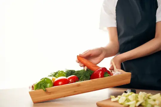 Повар в фартуке держит деревянный лоток со свежими овощами