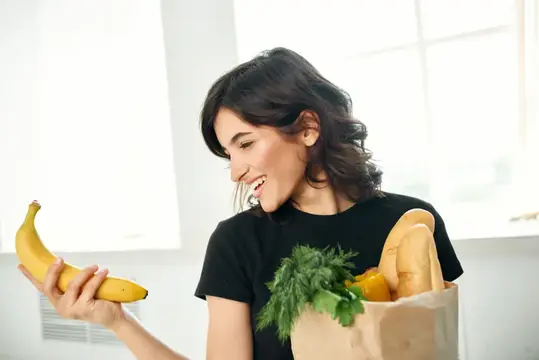 Жизнерадостная женщина с пакетом продуктов на кухне
