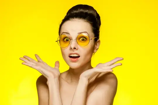 Удивлённая девушка в жёлтых круглых очках на ярком жёлтом фоне
