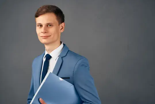 Молодой человек в синем костюме с папкой на сером фоне