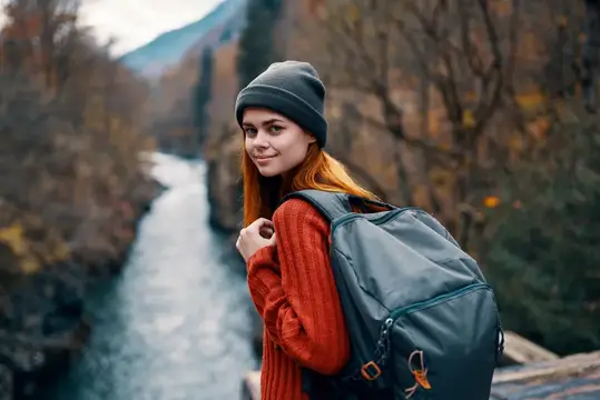 Рыжеволосая девушка с рюкзаком на фоне горной реки осенью