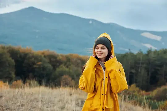 Улыбающаяся девушка в жёлтом дождевике на фоне осенних гор