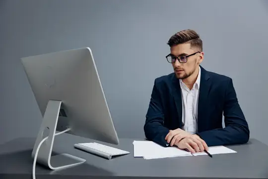 Молодой мужчина в очках и деловом костюме работает за компьютером в офисе