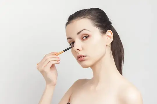 Веселая брюнетка с обнаженными плечами, кисть в руках, наносит крем