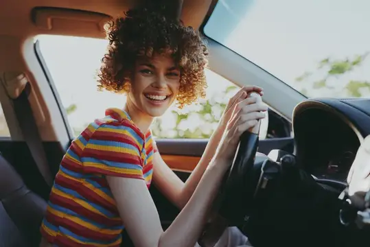 Улыбчивая кудрявая девушка за рулём автомобиля
