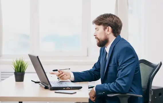 Бородатый мужчина в синем костюме работает за ноутбуком в офисе