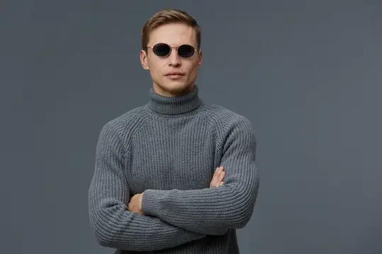 Крупный план модного мужчины в солнцезащитных очках и уютном сером свитере с высоким воротом