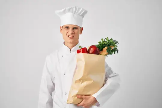 Шеф-повар с пакетом продуктов на кухне занимается приготовлением еды и работой