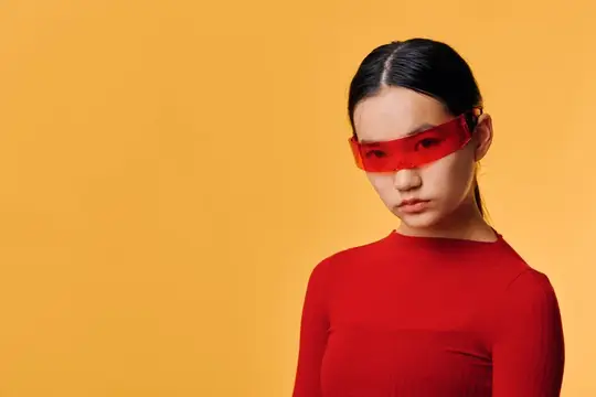 Портрет молодой женщины в красных солнцезащитных очках и соответствующем наряде с серьезным выражением лица на оранжевом фоне