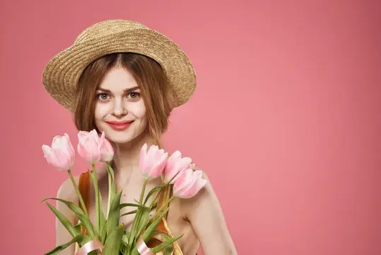 Молодая женщина в соломенной шляпе с букетом розовых тюльпанов на розовом фоне