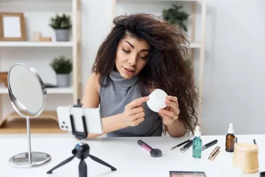 Кудрявая девушка записывает видео о косметике на смартфон