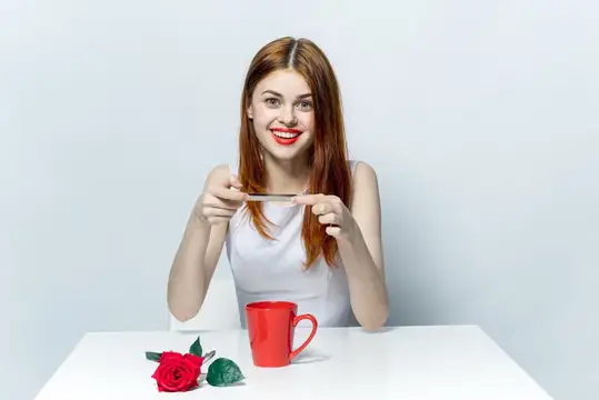 Женщина с телефоном в руках фотографирует стол с розой