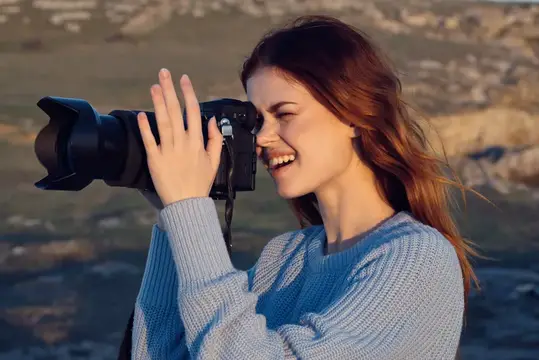 Улыбающаяся девушка с фотокамерой снимает на закате