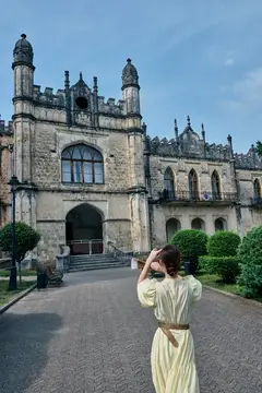 Девушка в светлом платье фотографирует старинный готический замок
