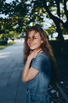 Улыбчивая девушка в джинсовом комбинезоне обернулась на аллее парка