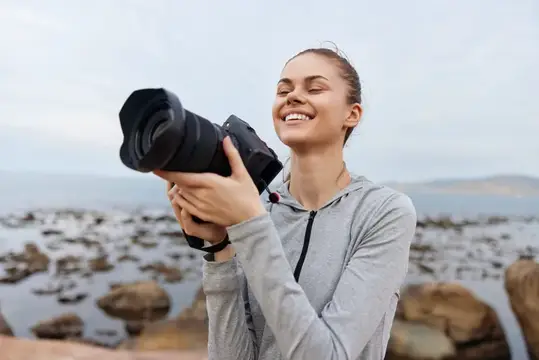 Улыбающаяся девушка с фотокамерой на каменистом берегу