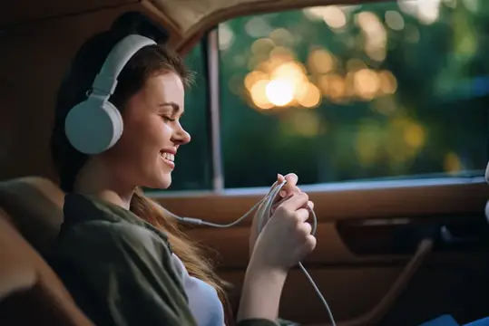 Улыбающаяся девушка в наушниках слушает музыку в машине