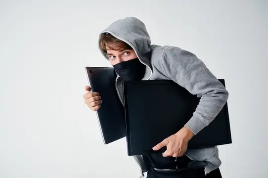 Мужчина в маске с капюшоном на голове занимается взломом на фоне света, что символизирует технологии и безопасность