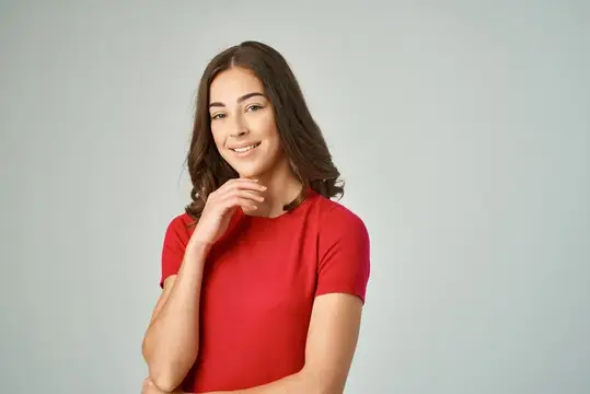 Улыбающаяся темноволосая девушка в красной футболке на сером фоне