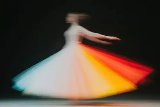 Динамичное и художественное размытие в движении танцовщицы, кружащейся в ярком платье с градиентом, передающее суть энергии, элегантности и театрального представления на темном фоне