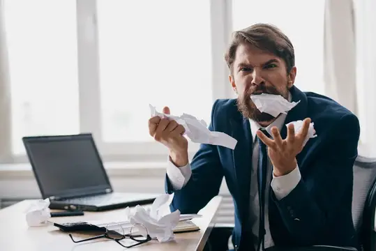 Менеджер работает за ноутбуком в офисе, испытывая эмоции недовольства от технологий