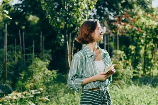 Молодая женщина с блокнотом гуляет по летнему саду