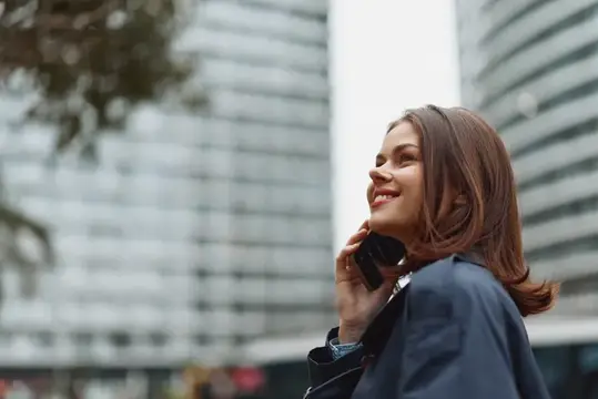 Улыбающаяся девушка говорит по телефону на фоне высоток