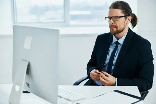 Мужчина с длинными волосами в очках работает за компьютером в офисе