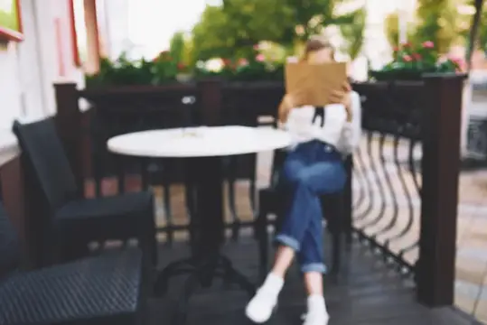 Девушка в джинсах читает книгу за столиком летнего кафе