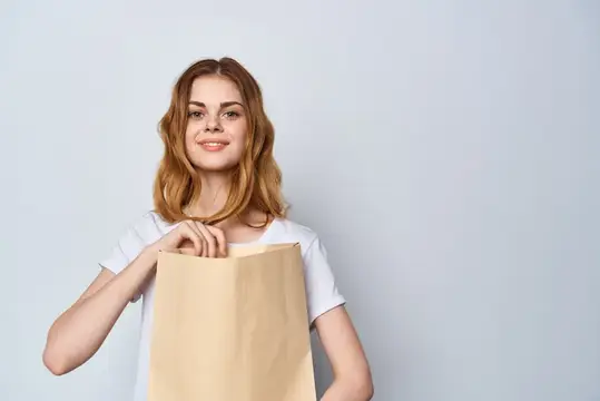 Молодая женщина с бумажным пакетом в руках на сером фоне