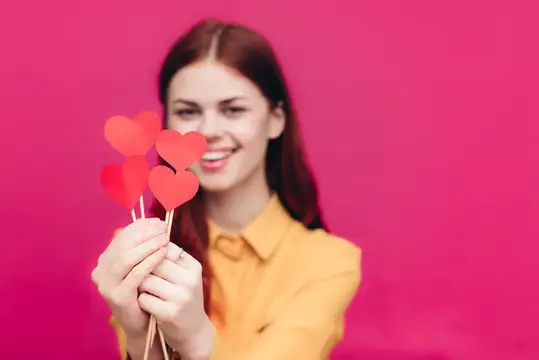Улыбающаяся девушка с бумажными сердечками на розовом фоне