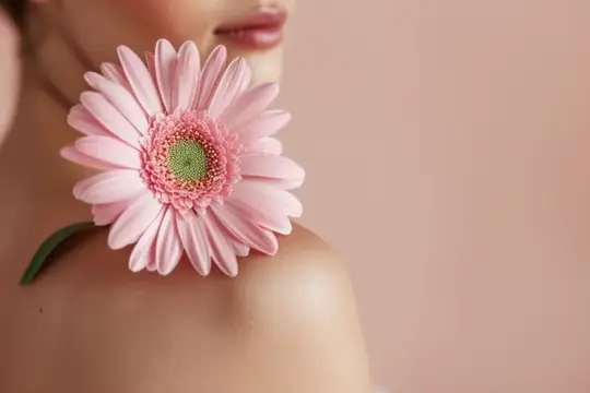 Нежное изображение женского плеча с лежащей на нем розовой герберой, окруженное мягким розовым тоном, который усиливает безмятежную эстетику